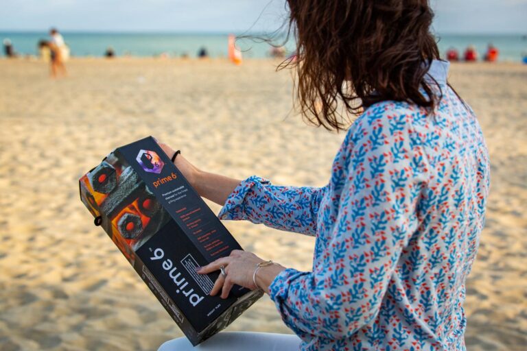 A woman sitting by the beach reading the back of a Prime6 Charcoal Box